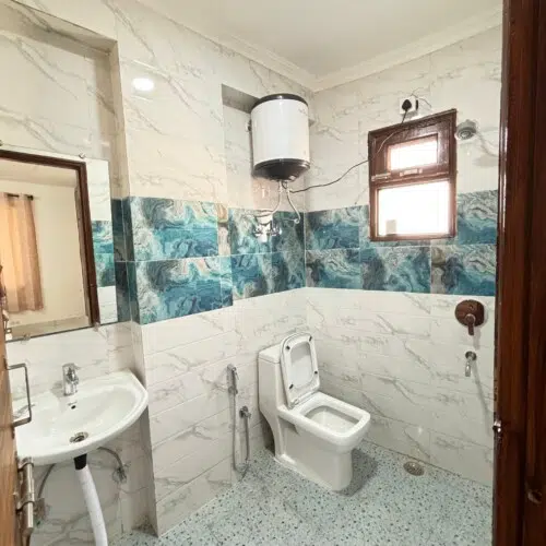 Modern attached bathroom with shower, western toilet, wash basin, and hot water facility at ValeStays serviced apartment